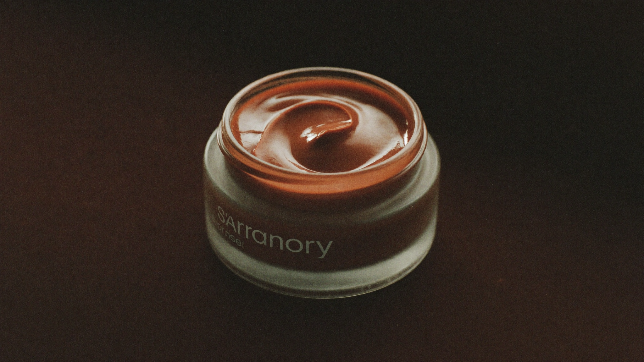 A single frosted jar in low warm lamplight against a deep, warm-brown background