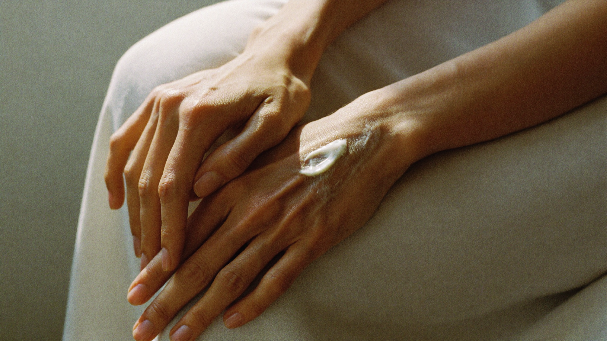 A pair of hands resting in warm natural light, skin texture visible and unretouched