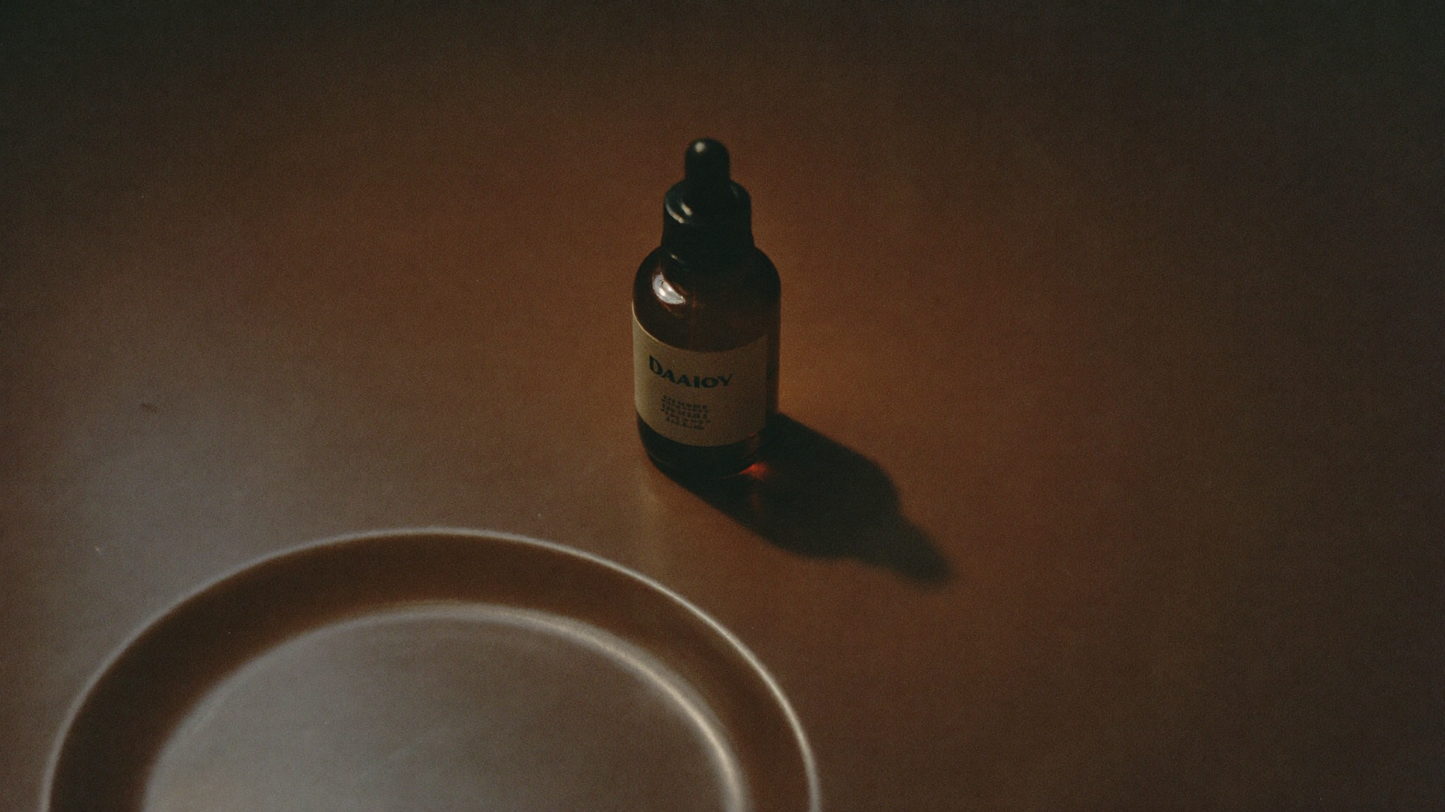 A single amber dropper bottle in low, warm evening light against a deep shadow