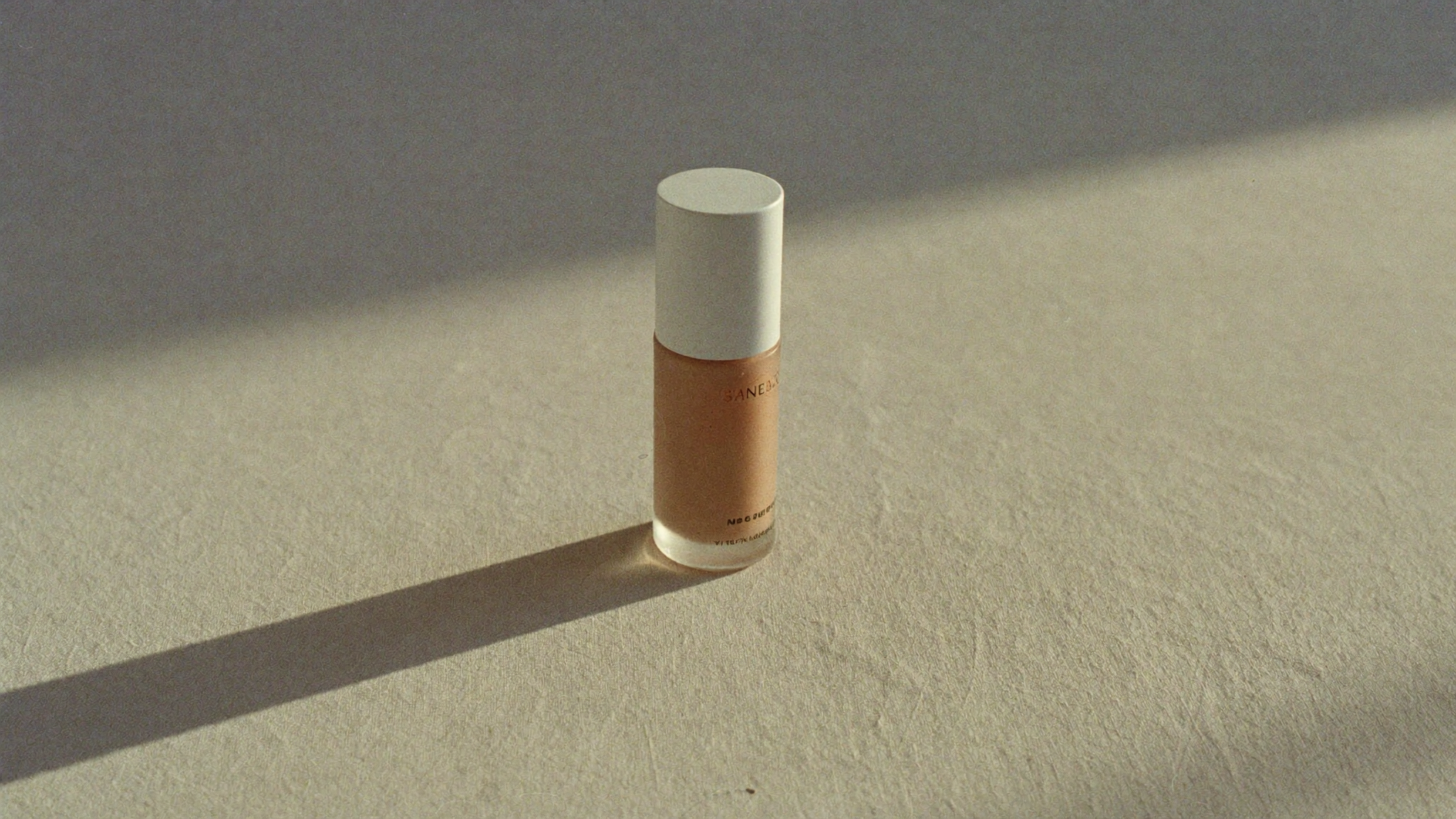 Soft morning light falling across a bone-coloured surface with a single frosted glass bottle