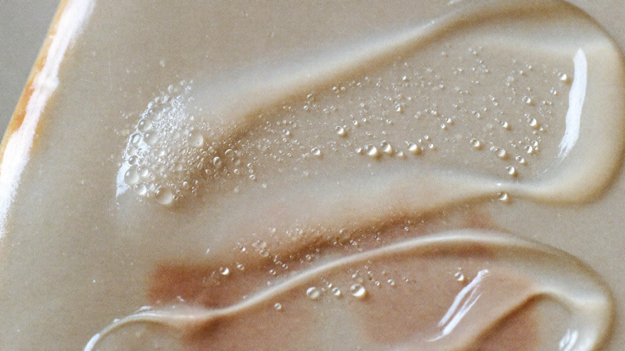 Translucent dewy gel texture with fine water droplets on a warm bone surface